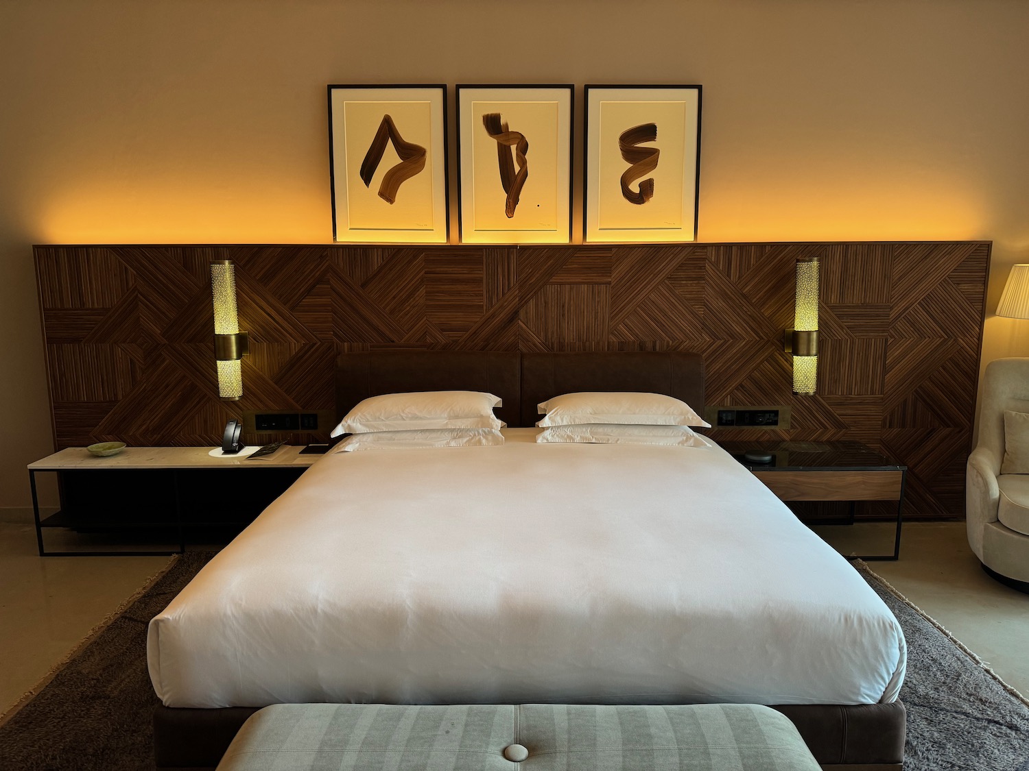 a bed with pillows and a bench in a room with art above it