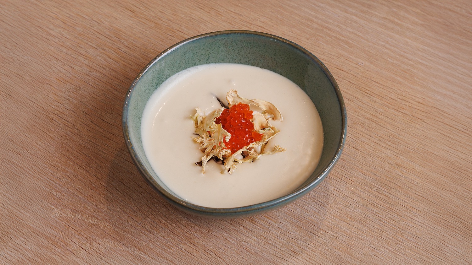 a bowl of soup with red caviar and dried herbs