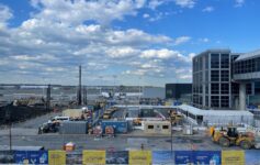 a construction site with a few buildings and a blue sky with clouds