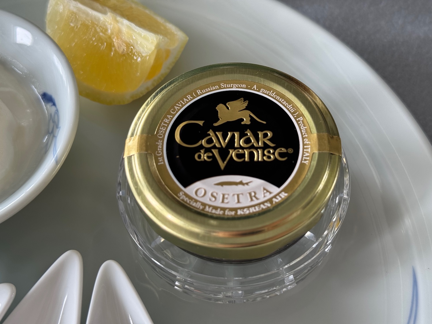 a small jar of caviar on a plate with a lemon wedge