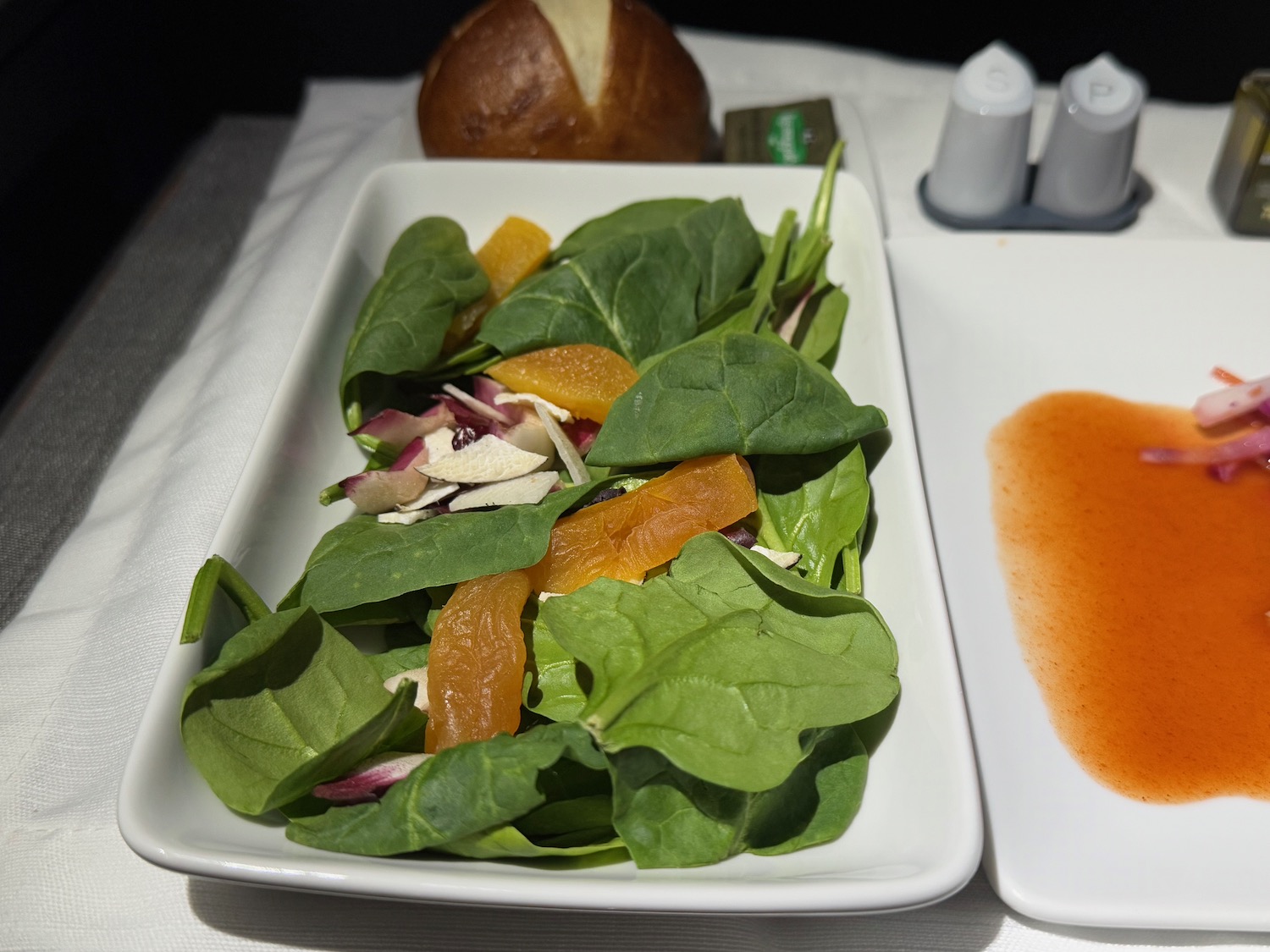 a plate of salad with orange slices and a roll