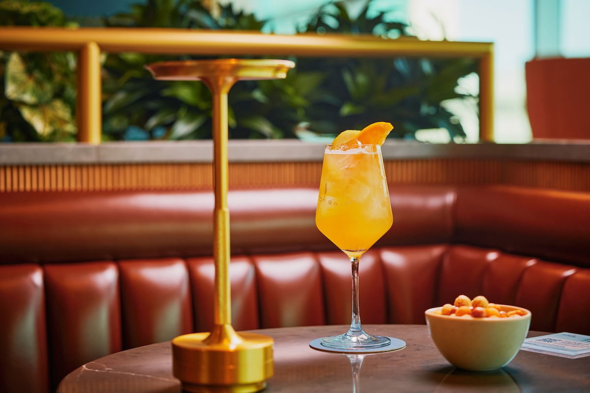 a glass of orange liquid next to a bowl of cereal