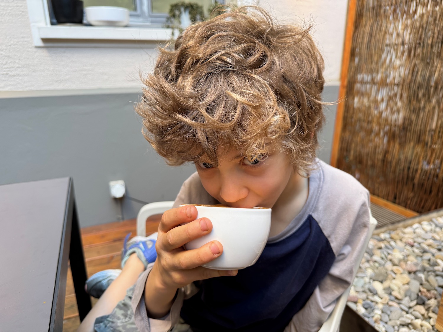 a boy sitting in a chair drinking from a white bowl