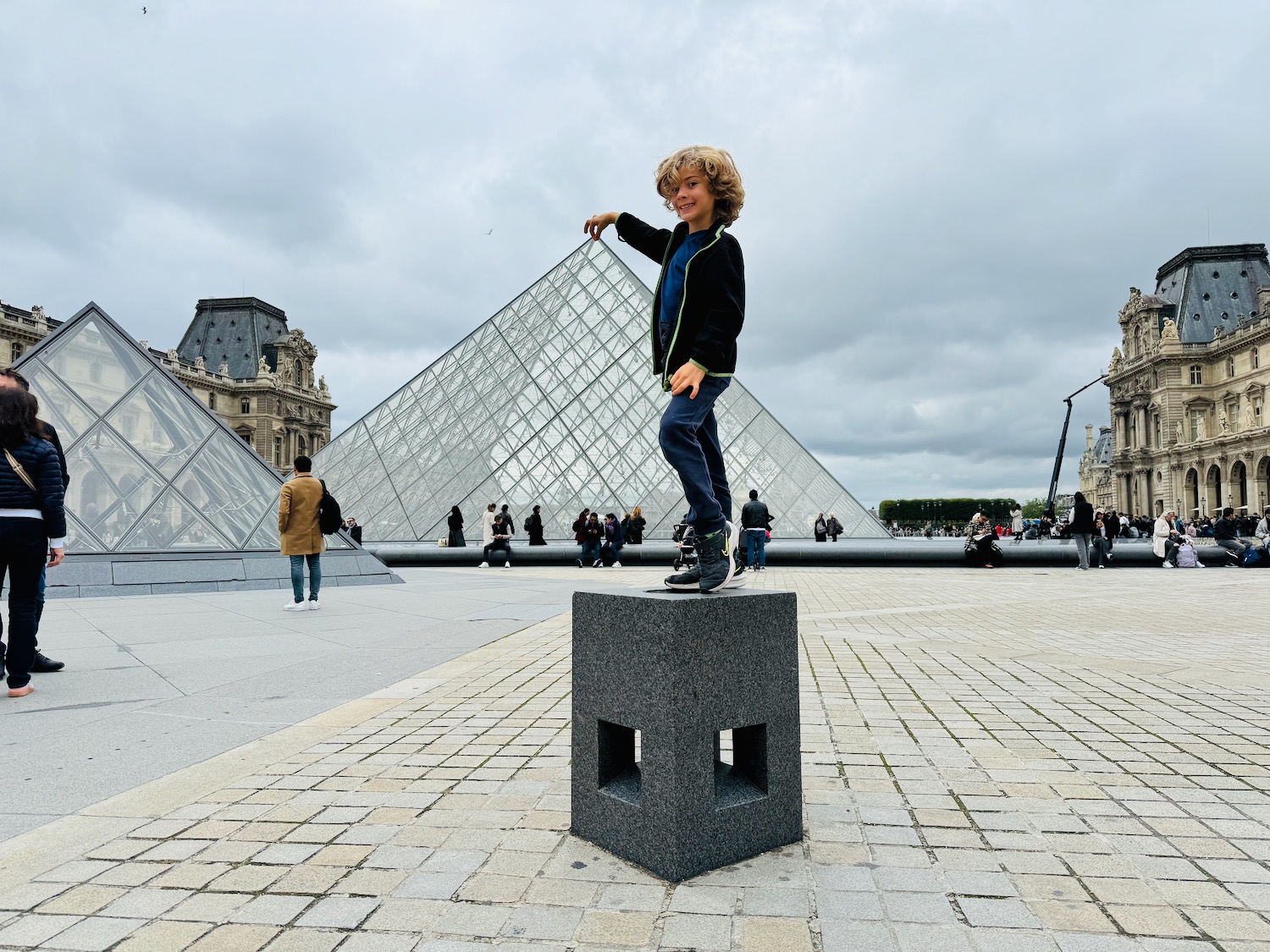 a boy standing on a stone block in front of a glass pyramid