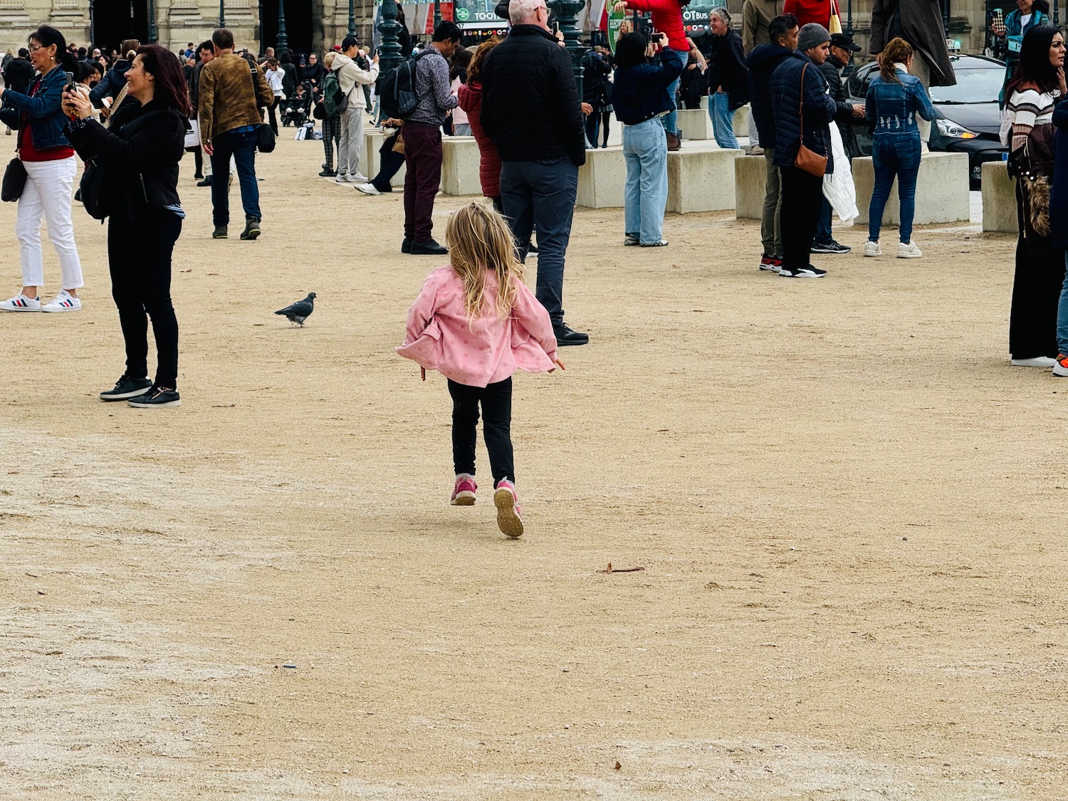 a girl walking in a dirt area with people and a building