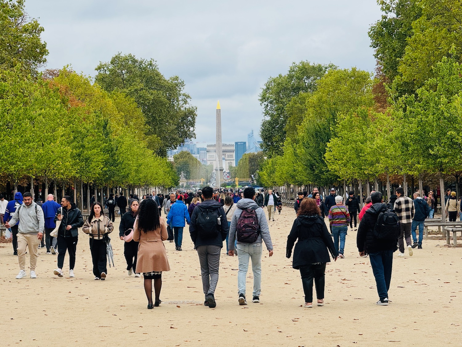 a group of people walking on a path with trees and a monument in the background