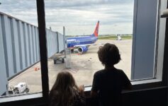 two children looking out a window at an airplane