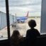 two children looking out a window at an airplane