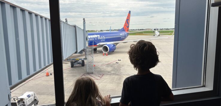 two children looking out a window at an airplane