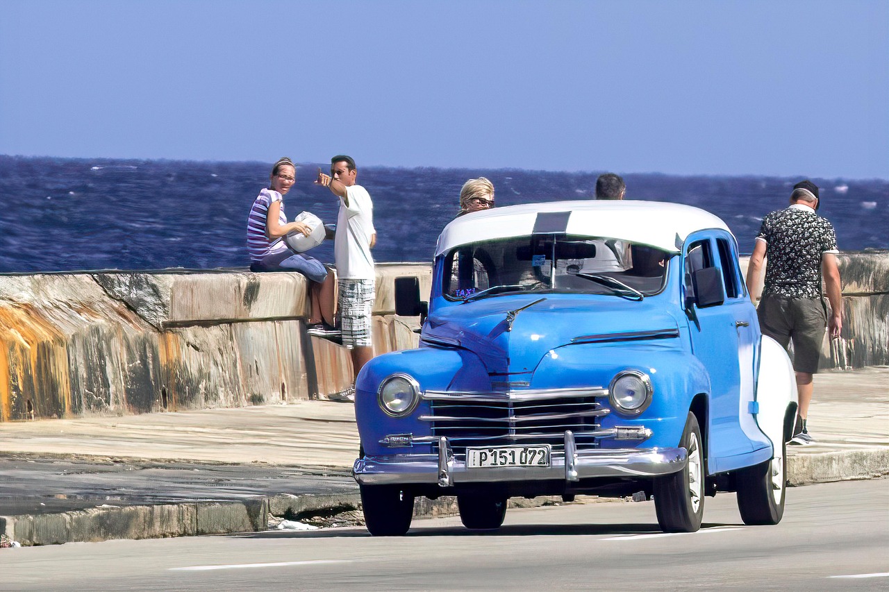 a blue car with people sitting on a wall