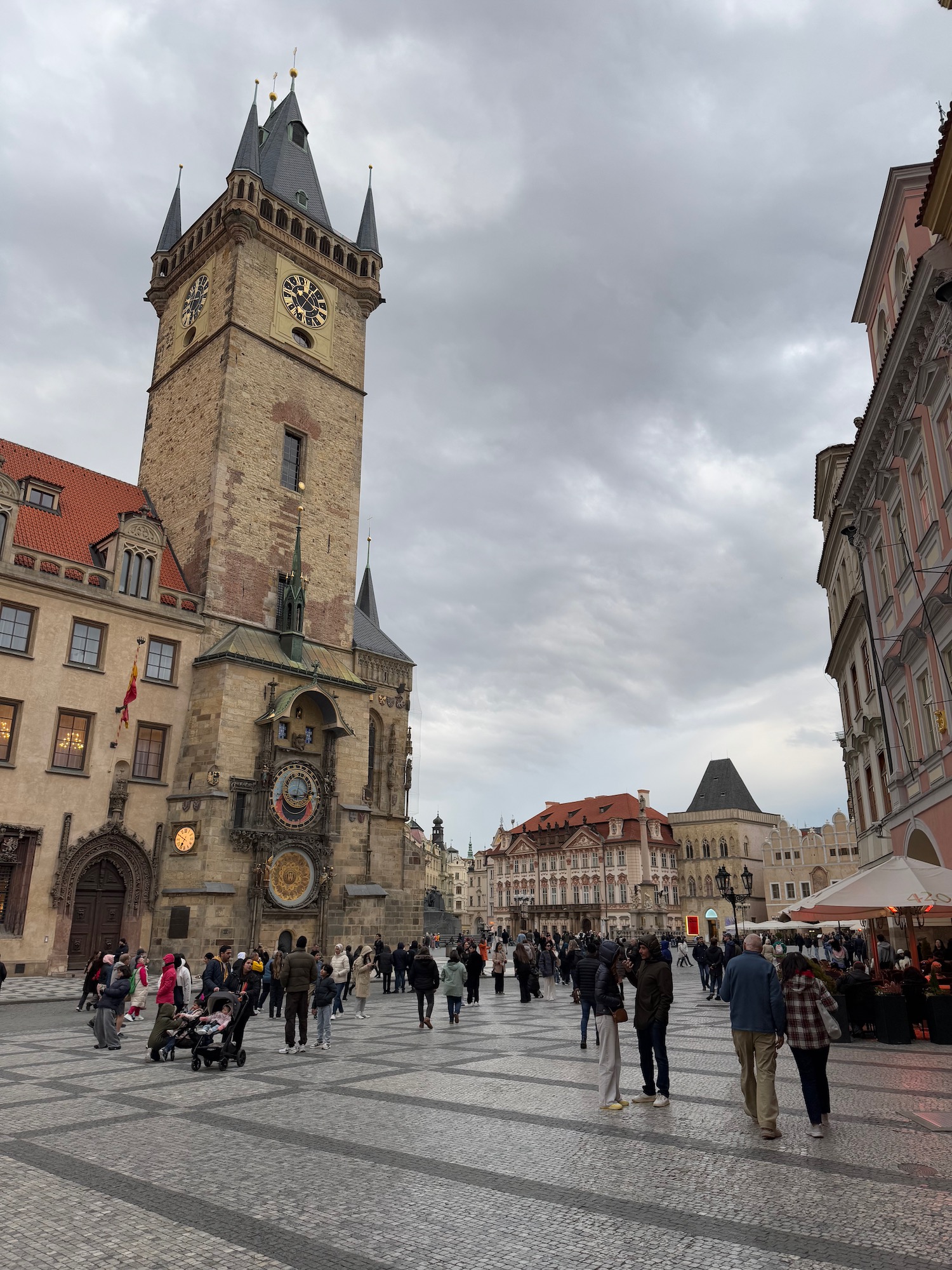 a group of people walking around a large building with Old Town Square in the background
