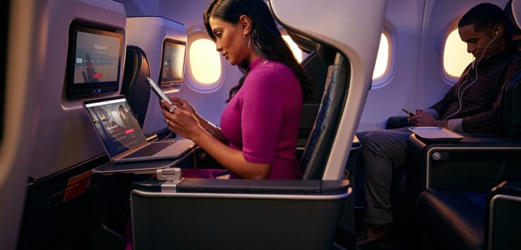 a woman sitting in an airplane with a laptop and a phone