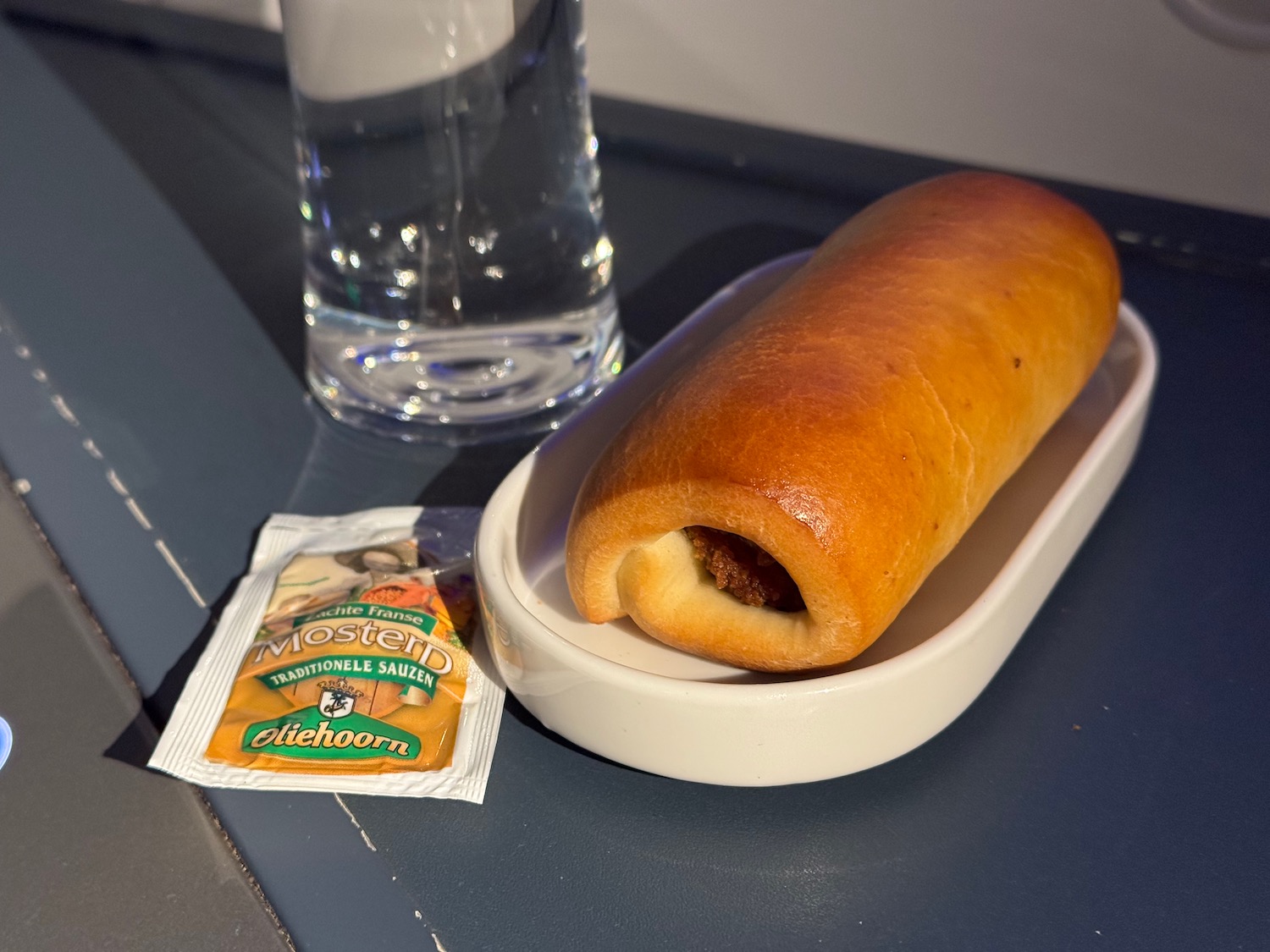 a hot dog on a plate next to a glass of water