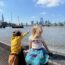 a boy and girl standing on a brick wall by water and a city