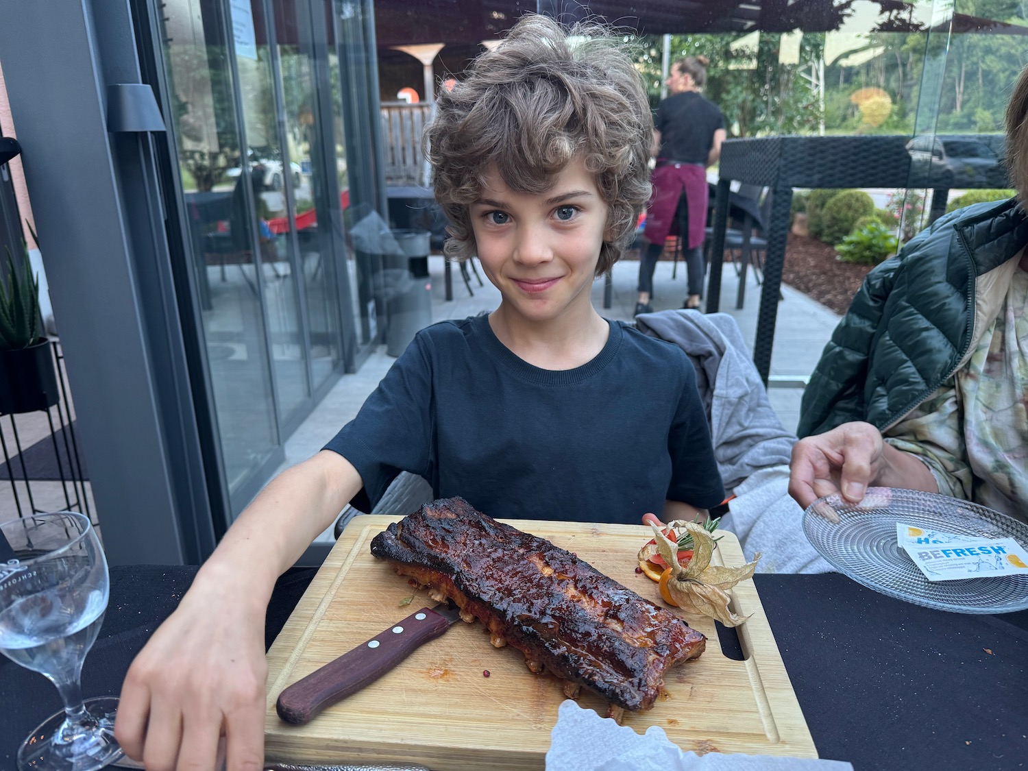 a boy sitting at a table with a plate of ribs
