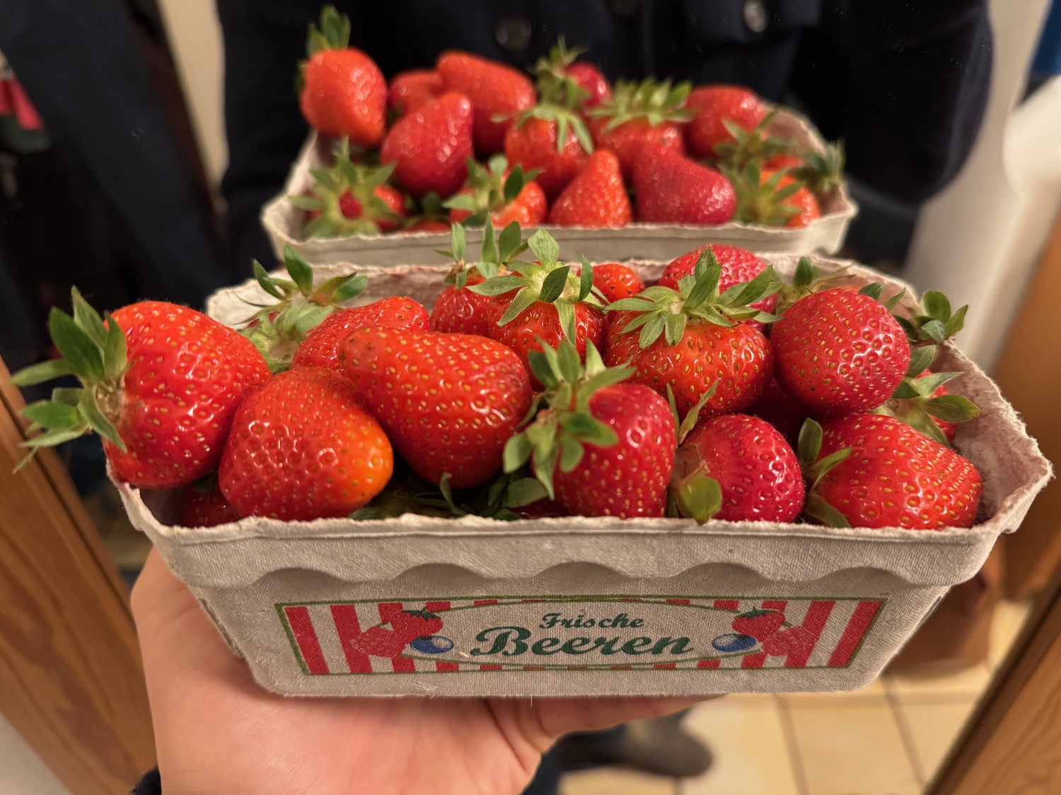 a hand holding a carton of strawberries