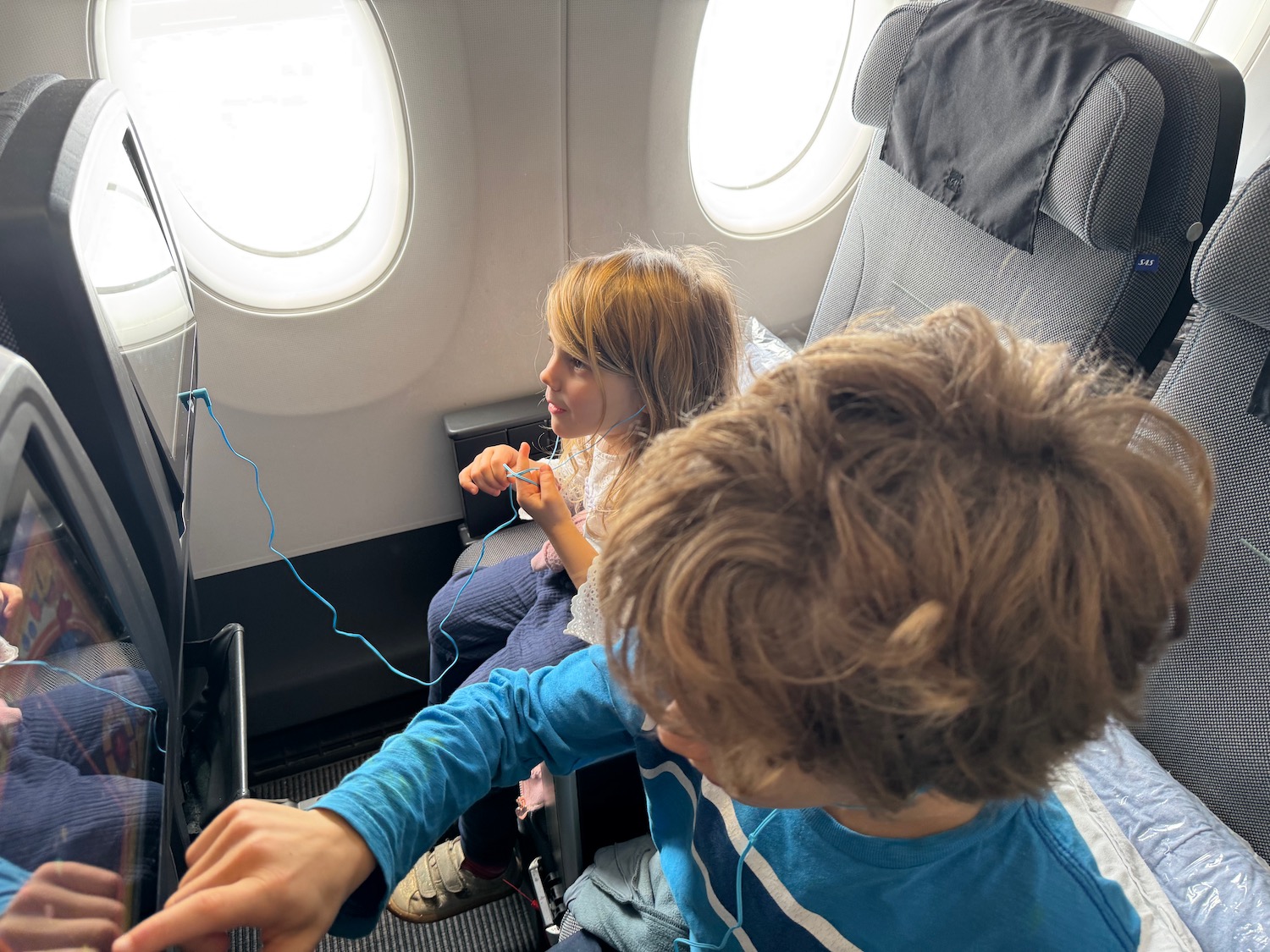 a boy and girl sitting on an airplane with a cord attached to the screen