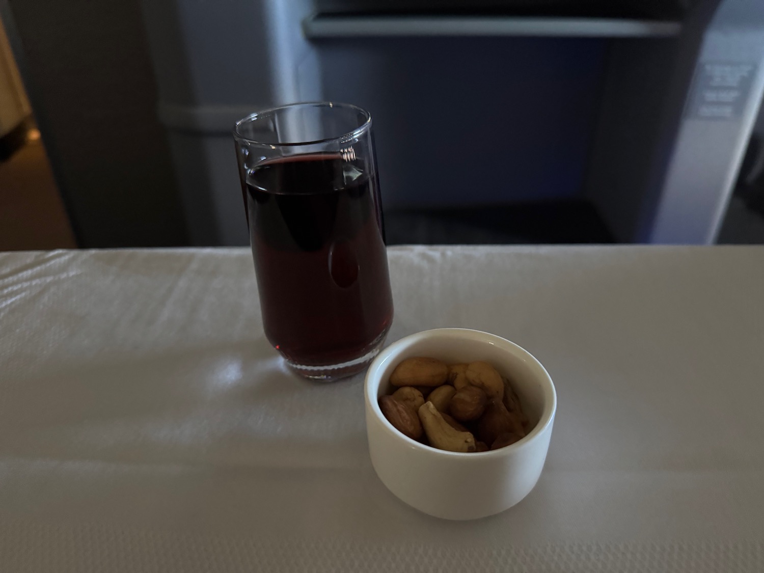 a glass of red liquid next to a bowl of nuts