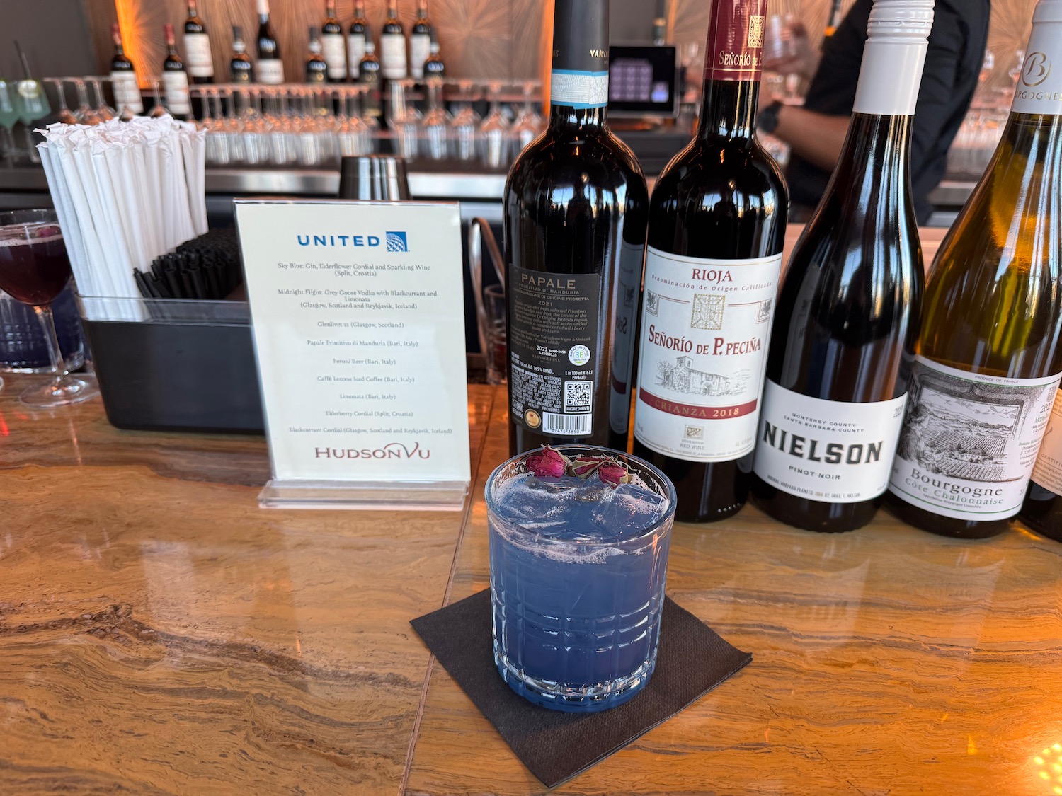 a glass of blue liquid next to bottles of wine