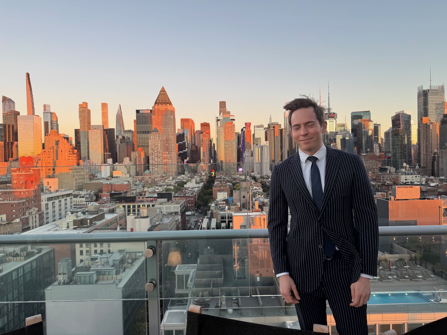 a man in a suit standing on a balcony with a city in the background