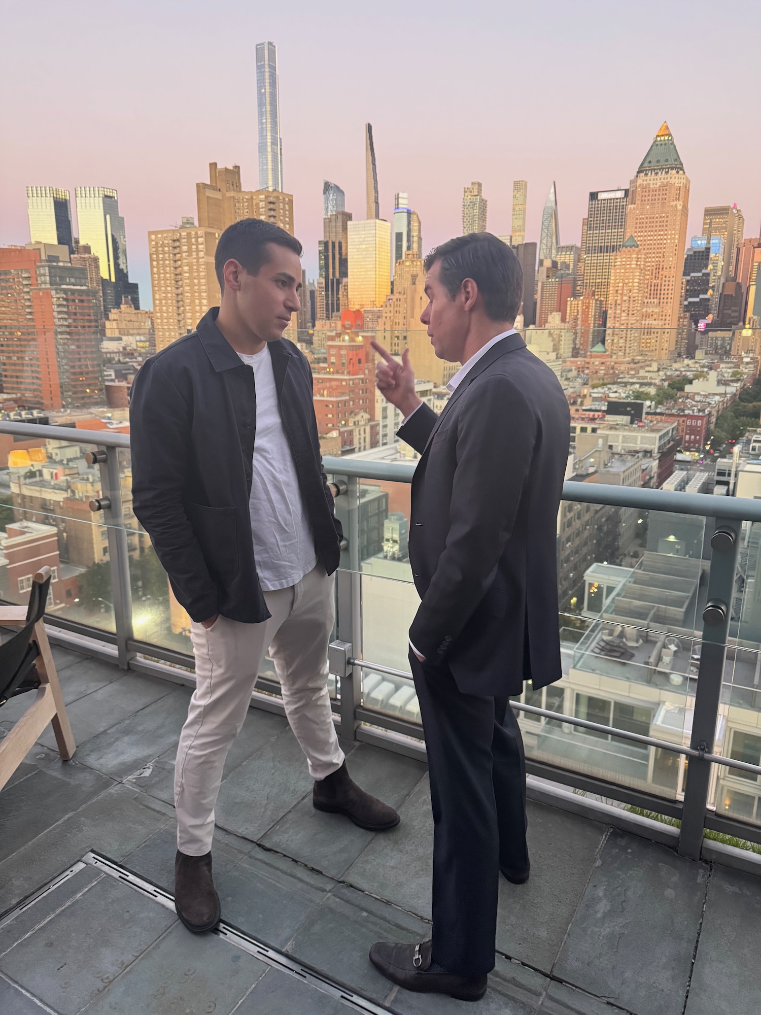 two men standing on a balcony with a city in the background