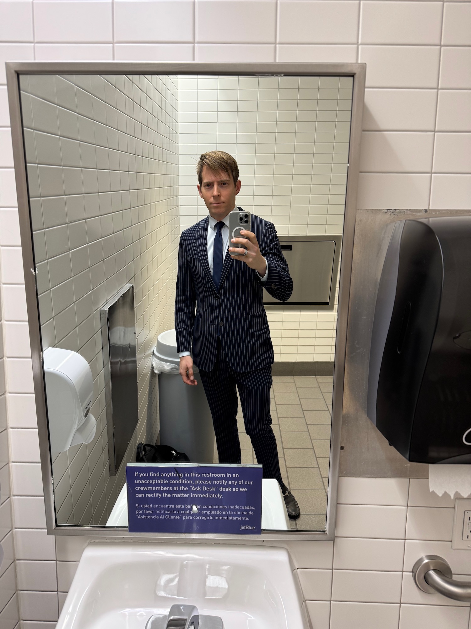 a man in a suit taking a selfie in a bathroom mirror