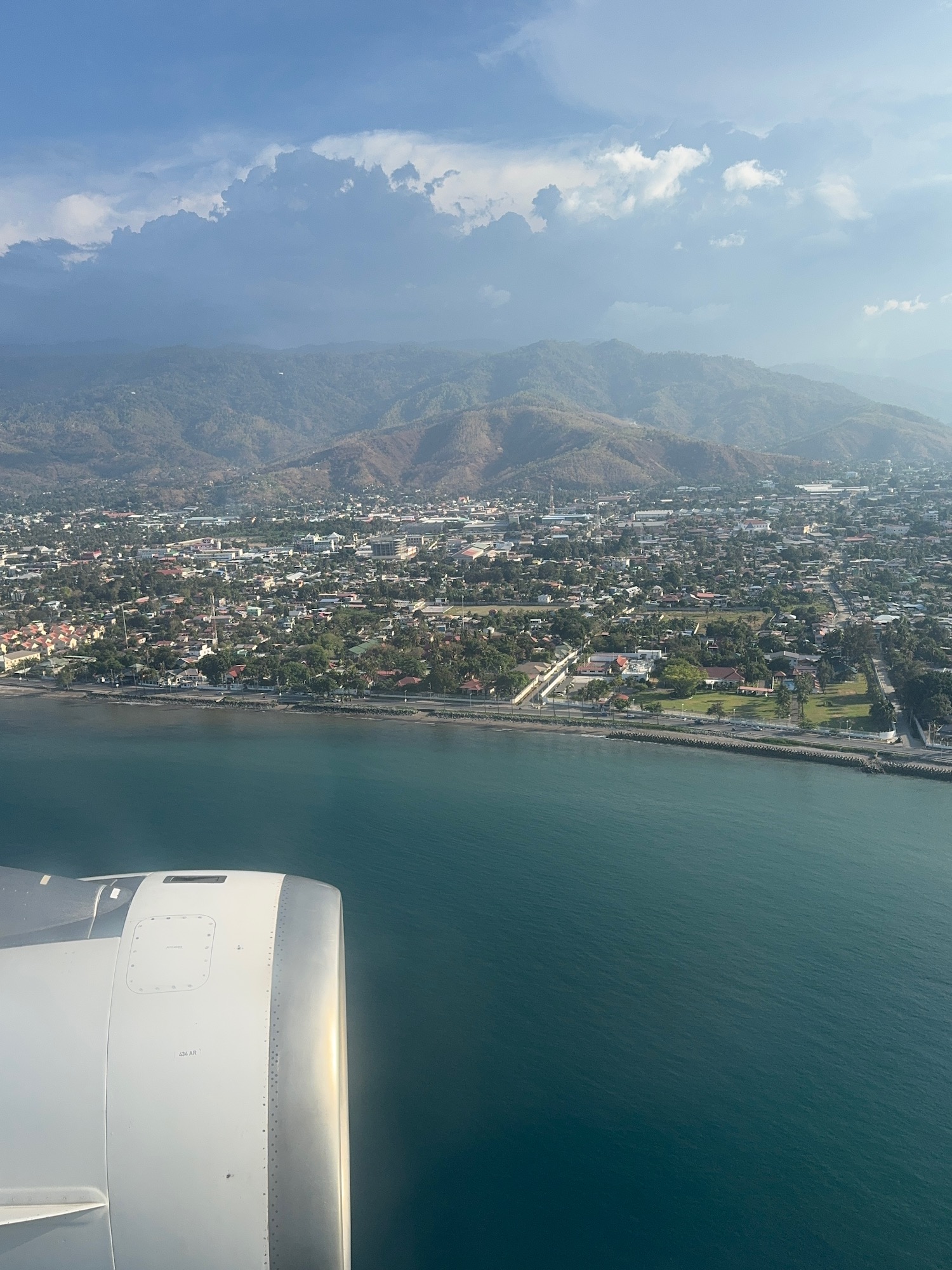 an airplane wing over a body of water with a city and mountains in the background