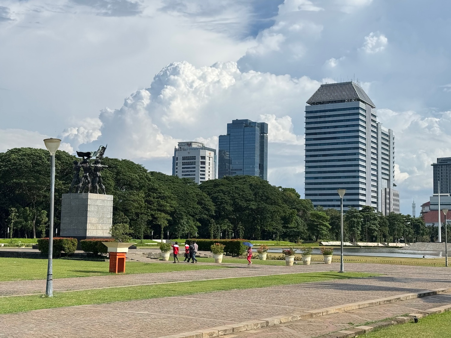 a group of people walking in a park with a statue and trees