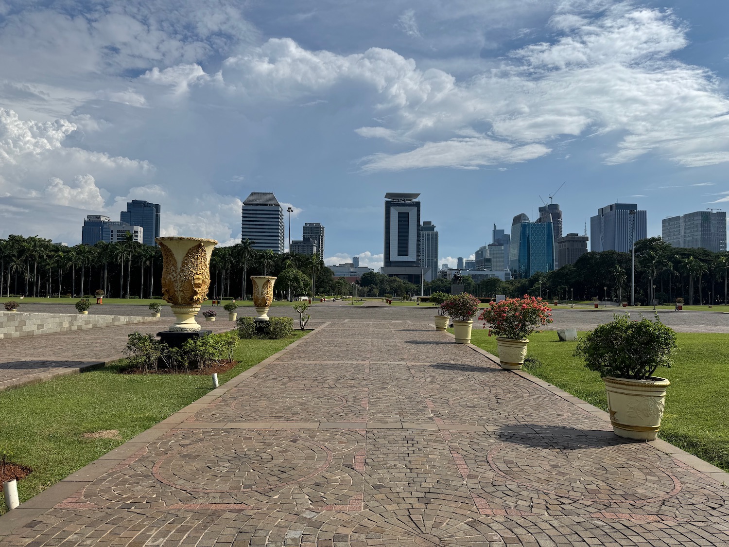 a brick walkway with plants and flowers in pots in front of a city
