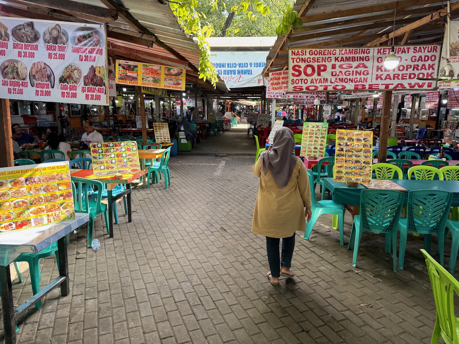 a woman walking down a street with tables and chairs