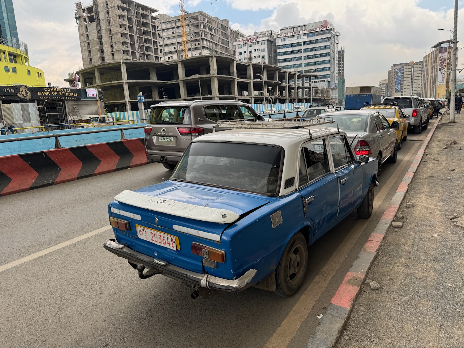 a blue car on a road with buildings in the background