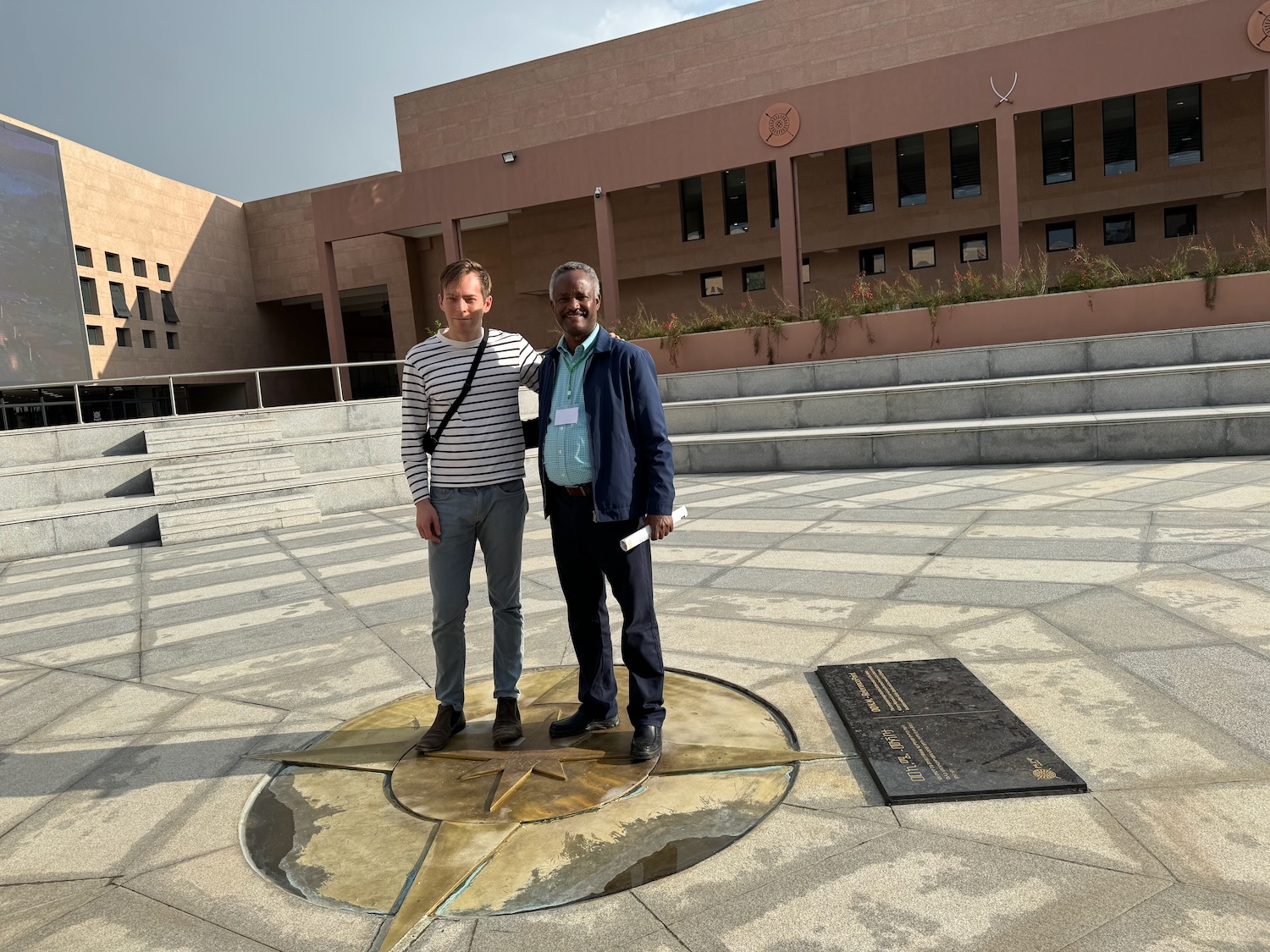 two men standing on a circular metal surface in front of a building
