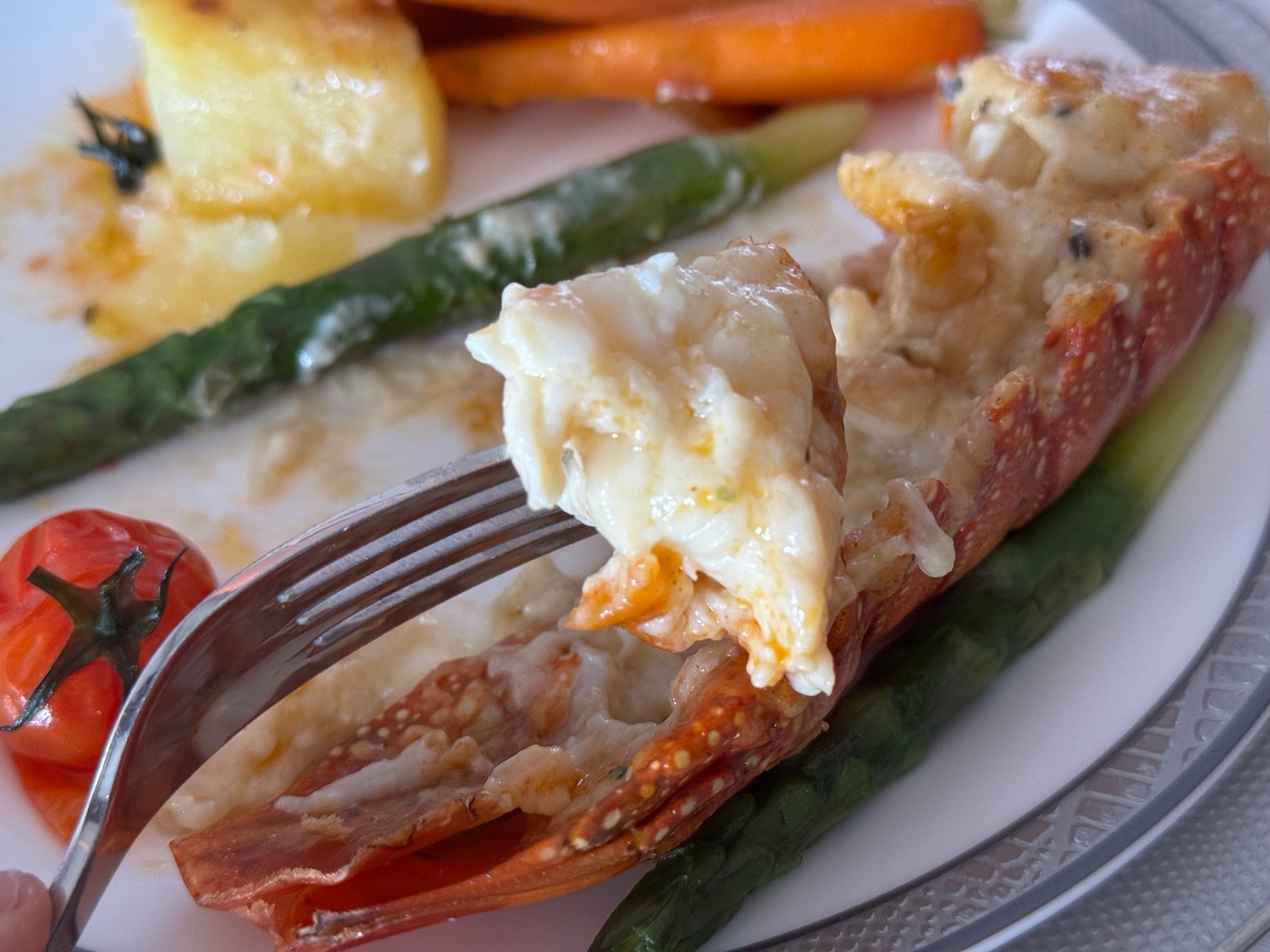 a lobster tail with a fork on a plate with vegetables