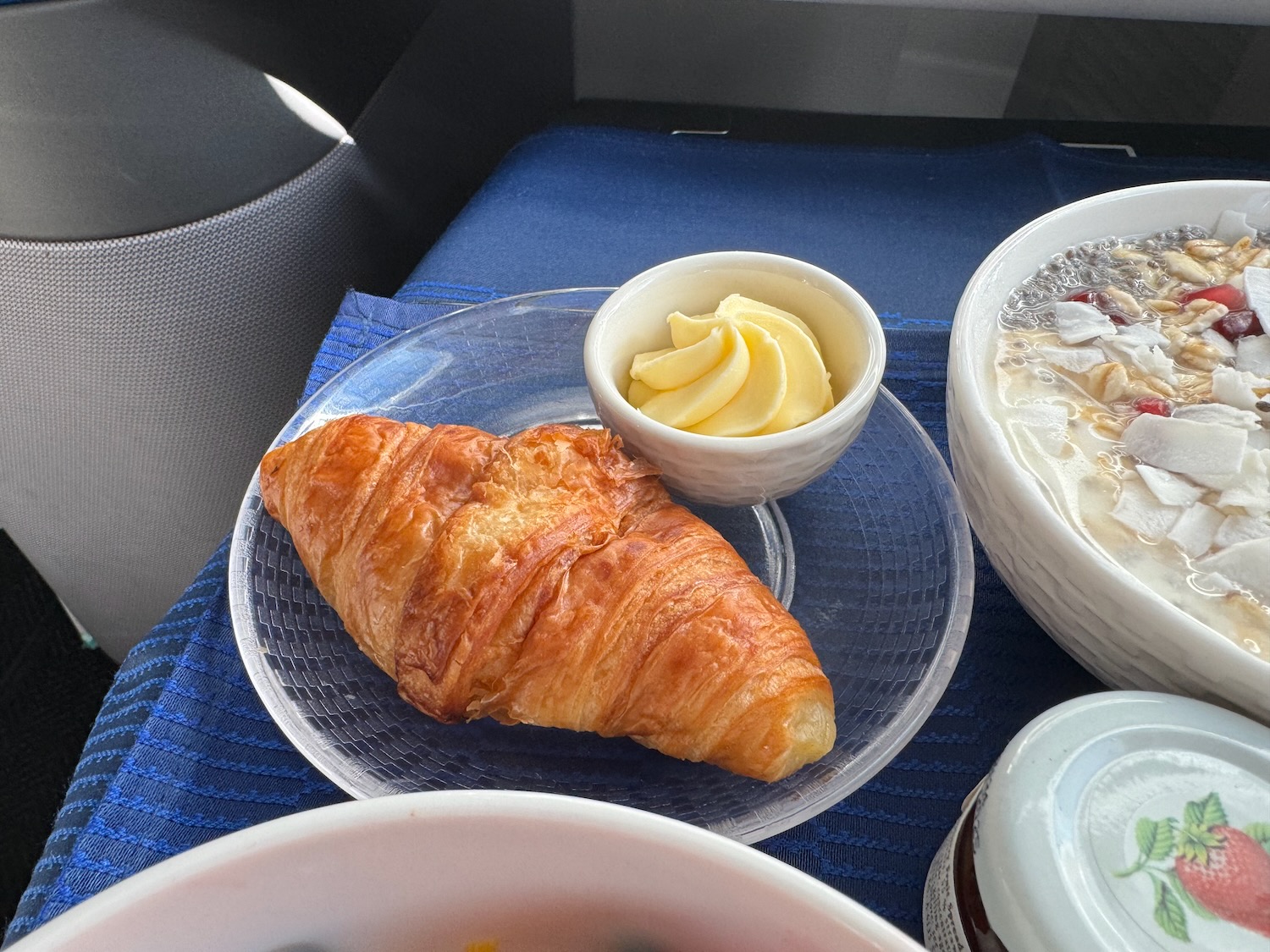 a croissant on a plate with butter and a bowl of soup