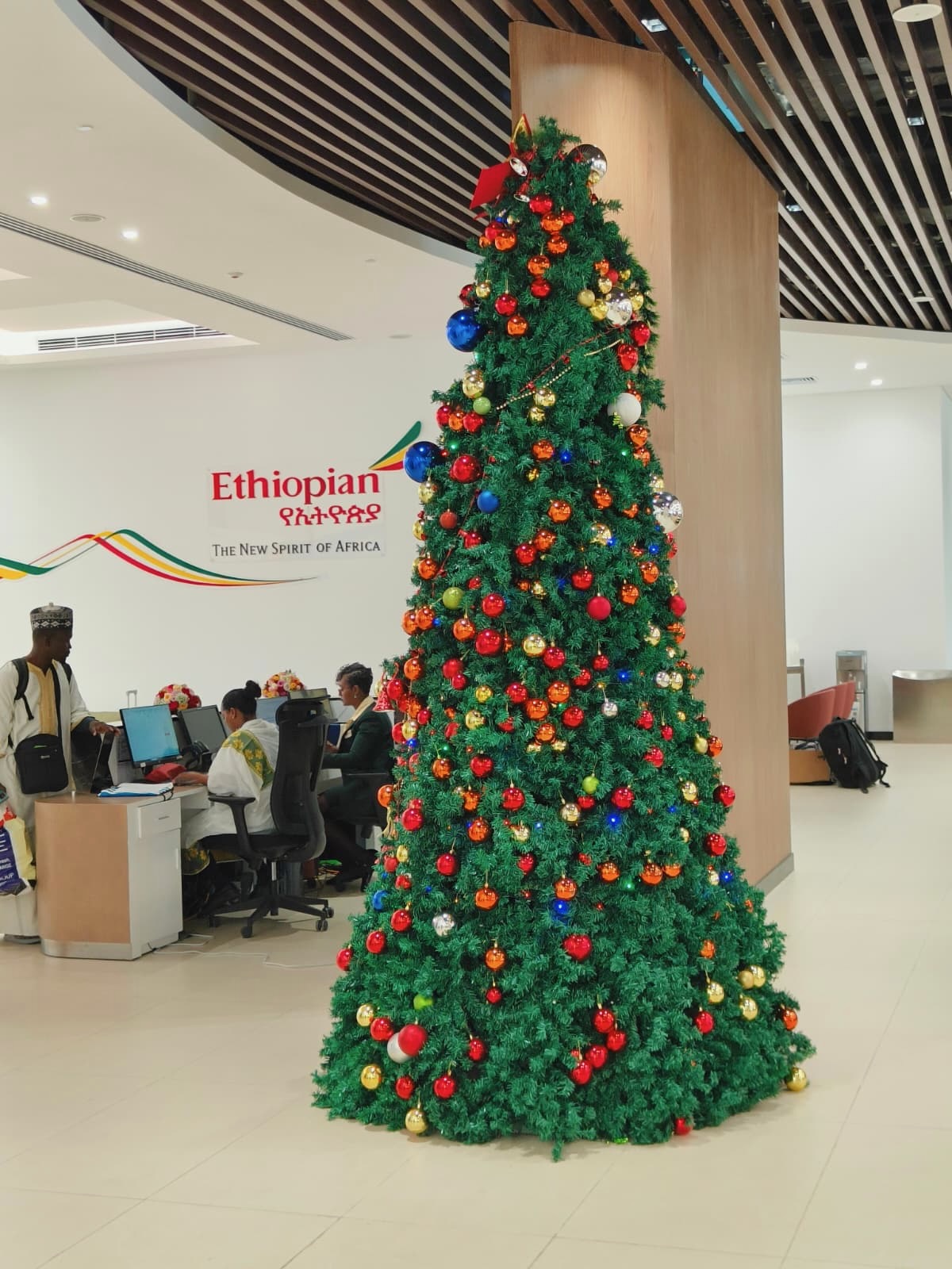 a tree with ornaments and lights in a room with people in the background