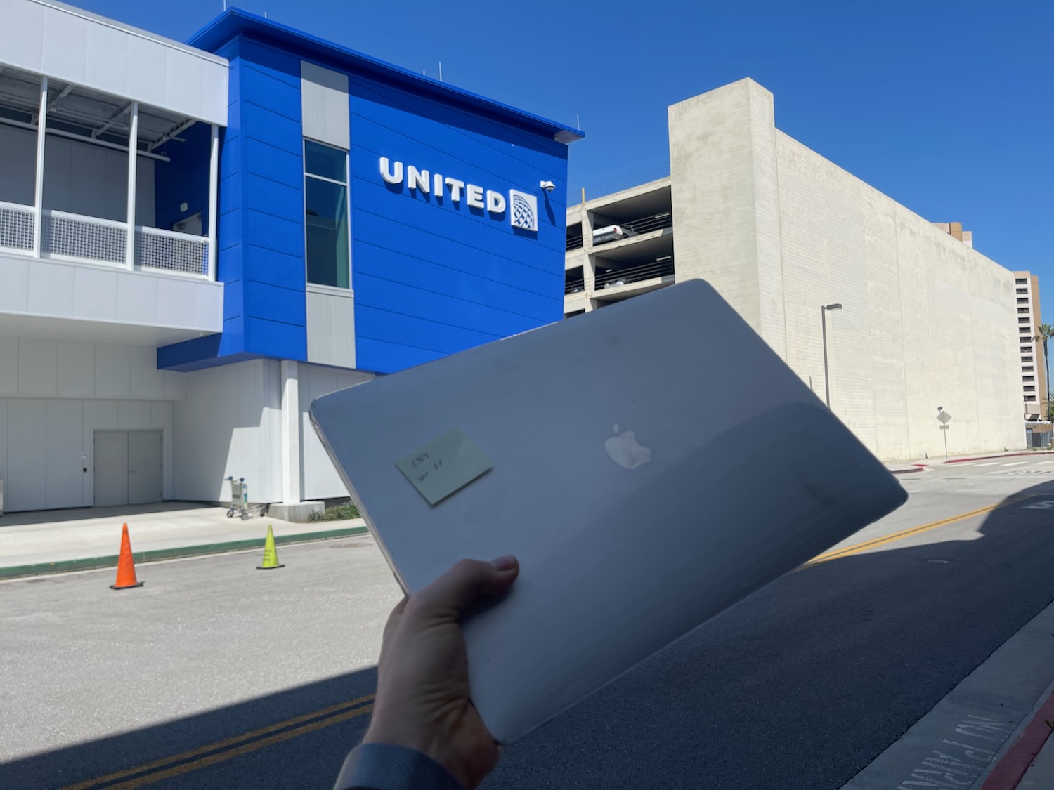 a hand holding a laptop in front of a blue building