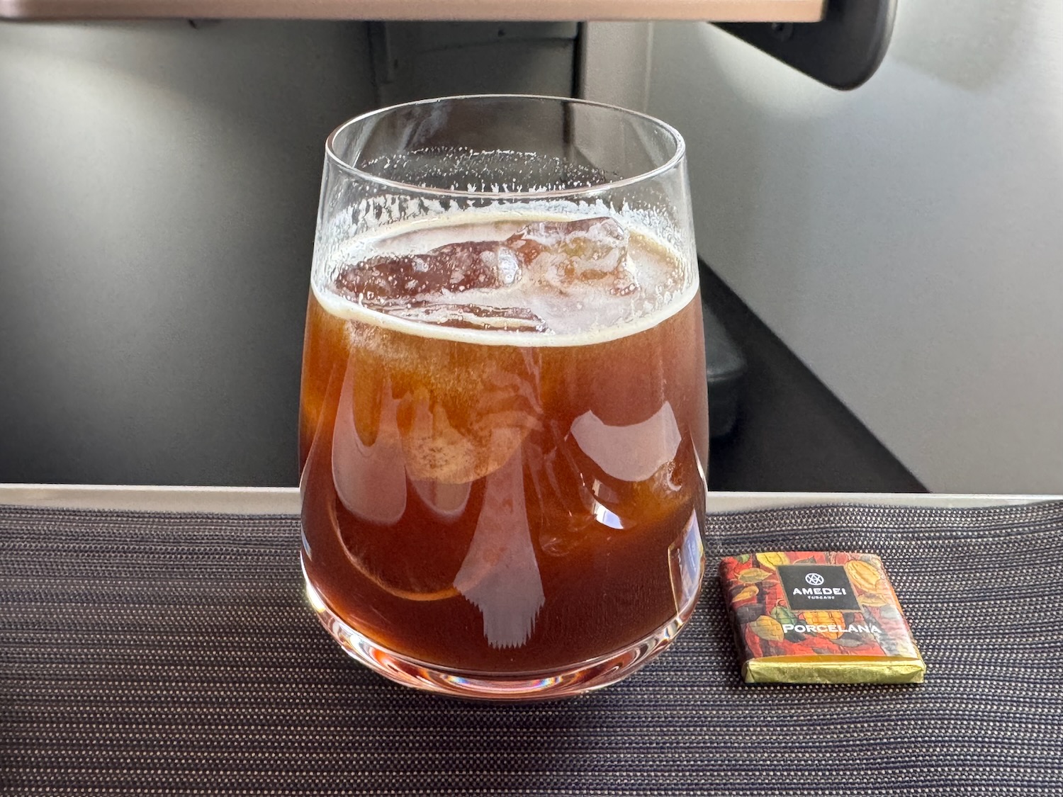 a glass of brown liquid next to a small candy