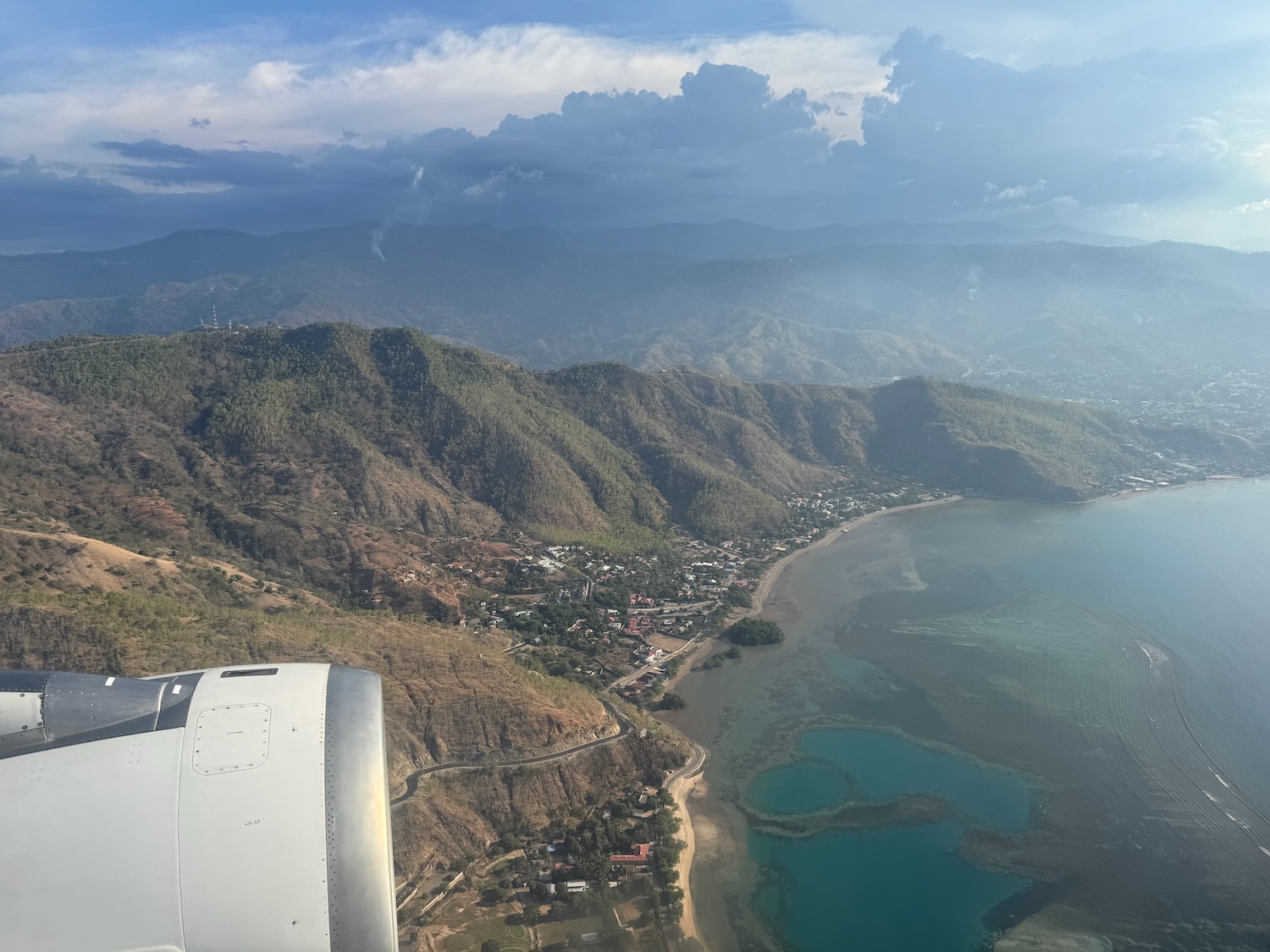 an airplane wing over a body of water and mountains