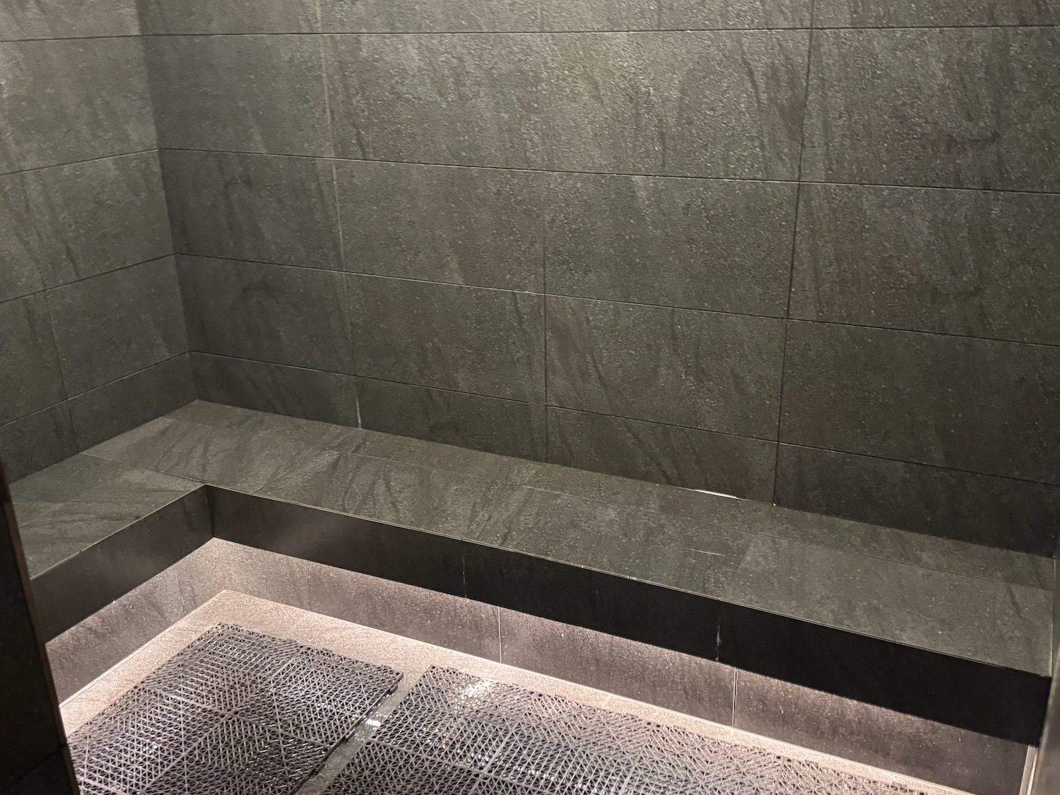 a grey tiled shower with a metal grate