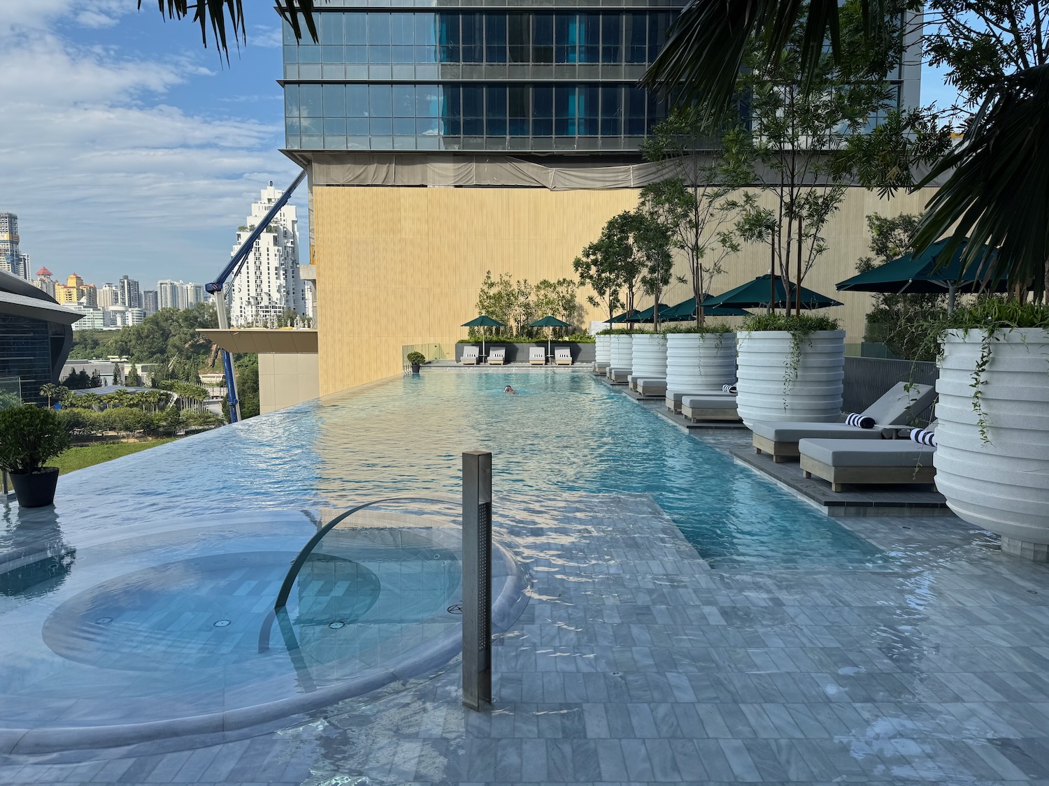 a pool with a jacuzzi and trees and a building in the background